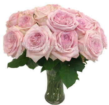 A lush bouquet of Pink Invitation Pink Garden Roses in a glass vase, showcasing their soft pink color and ruffled petal structure.