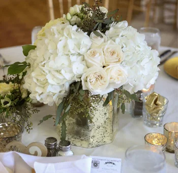 White hydrangea and rose wedding centerpiece with greenery in glass vase for elegant reception table decor.