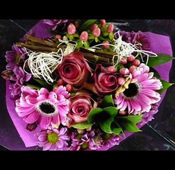 Charming Mother's Day flower centerpiece with pink roses, purple daisies, greenery, and decorative white twine, arranged in a purple wrap with rustic accents.