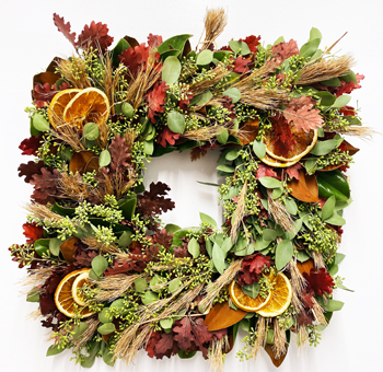 Full view of the Thanksgiving Wreath - Spice Things Up, featuring a square design with orange slices, dried wheat, autumn leaves, and lush greenery. Perfect for seasonal décor.