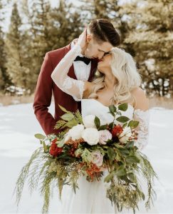 Couple having a Christmas wedding theme outdoors holding Christmas flowers.