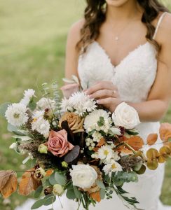 Bride holding bouquet with fall wedding flowers.