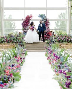 Newlywed couple with backdrop of colorful, luxurious wedding flowers.