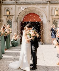Newlywed couple with surrounded with peach colored flowers and green accents