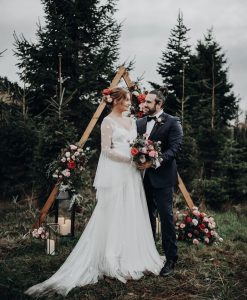 Newlywed couple on Christmas tree farm with wedding bouquet.
