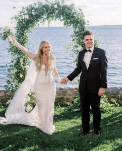Newlywed couple by seaside with bouquet of flowers.