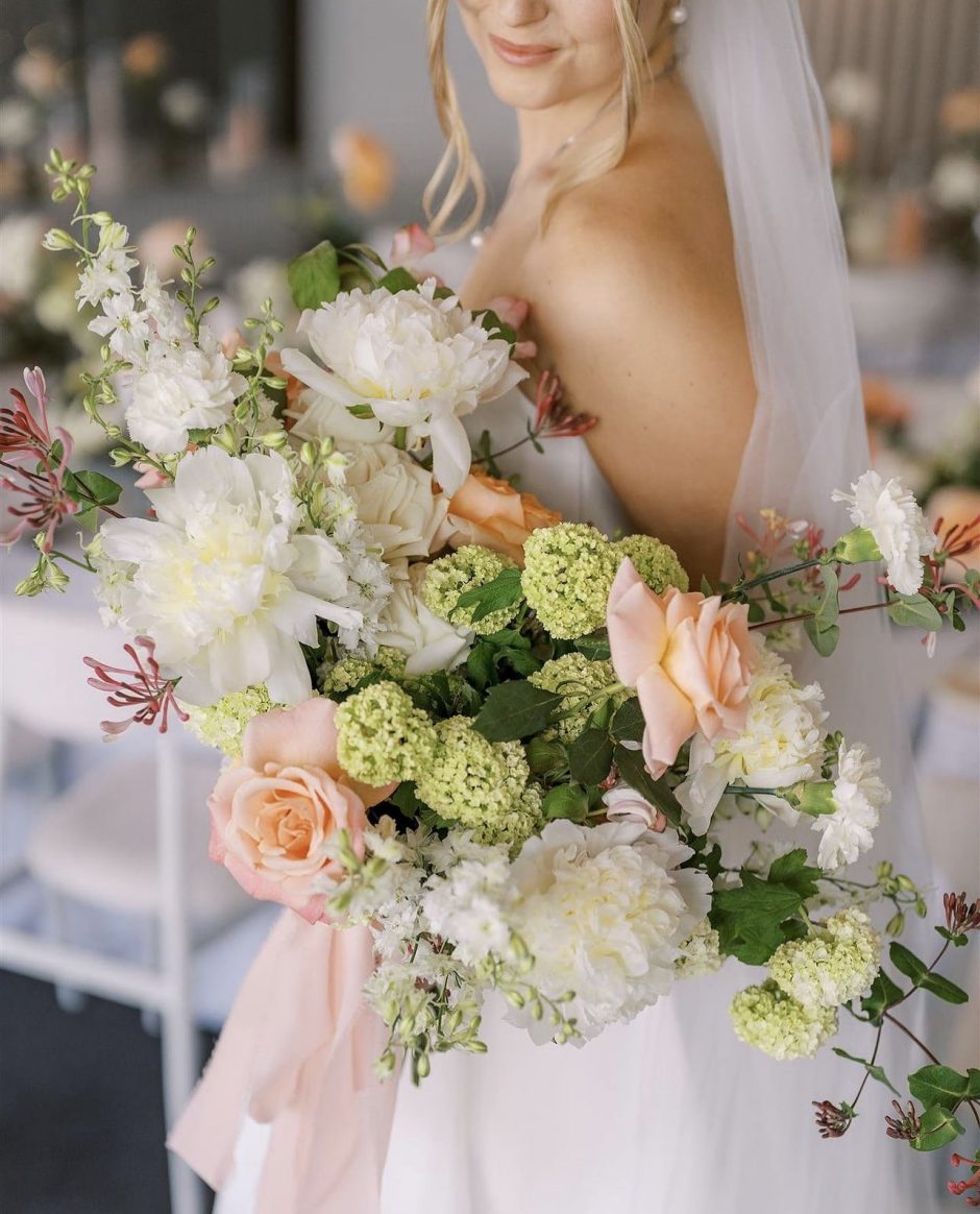Bride holding bouquet of green hydrangeas, peach roses, and white peonies.