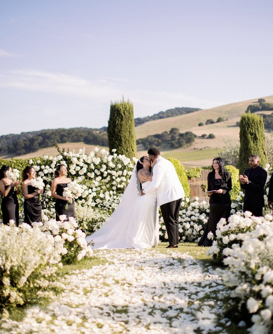 Newlywed couple surrounded with aisle of white flowers.