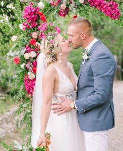 Newlywed couple kissing in front of wedding arch of bougainvilleas.