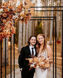 Newlywed couple outdoors with fall wedding flowers.