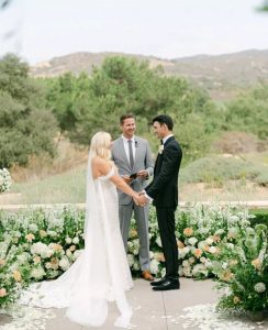 Couple repeating vows with background of white flowers.