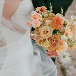 Bride holding bouquet with peach, brown, and white flowers.