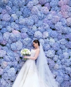 Bride surrounded by flower wall of blue hydrangeas.