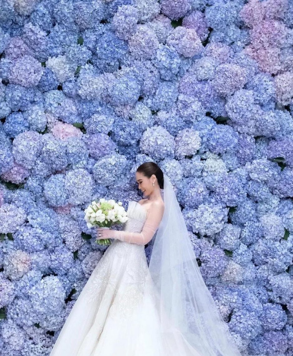 Bride surrounded by flower wall of blue hydrangeas.