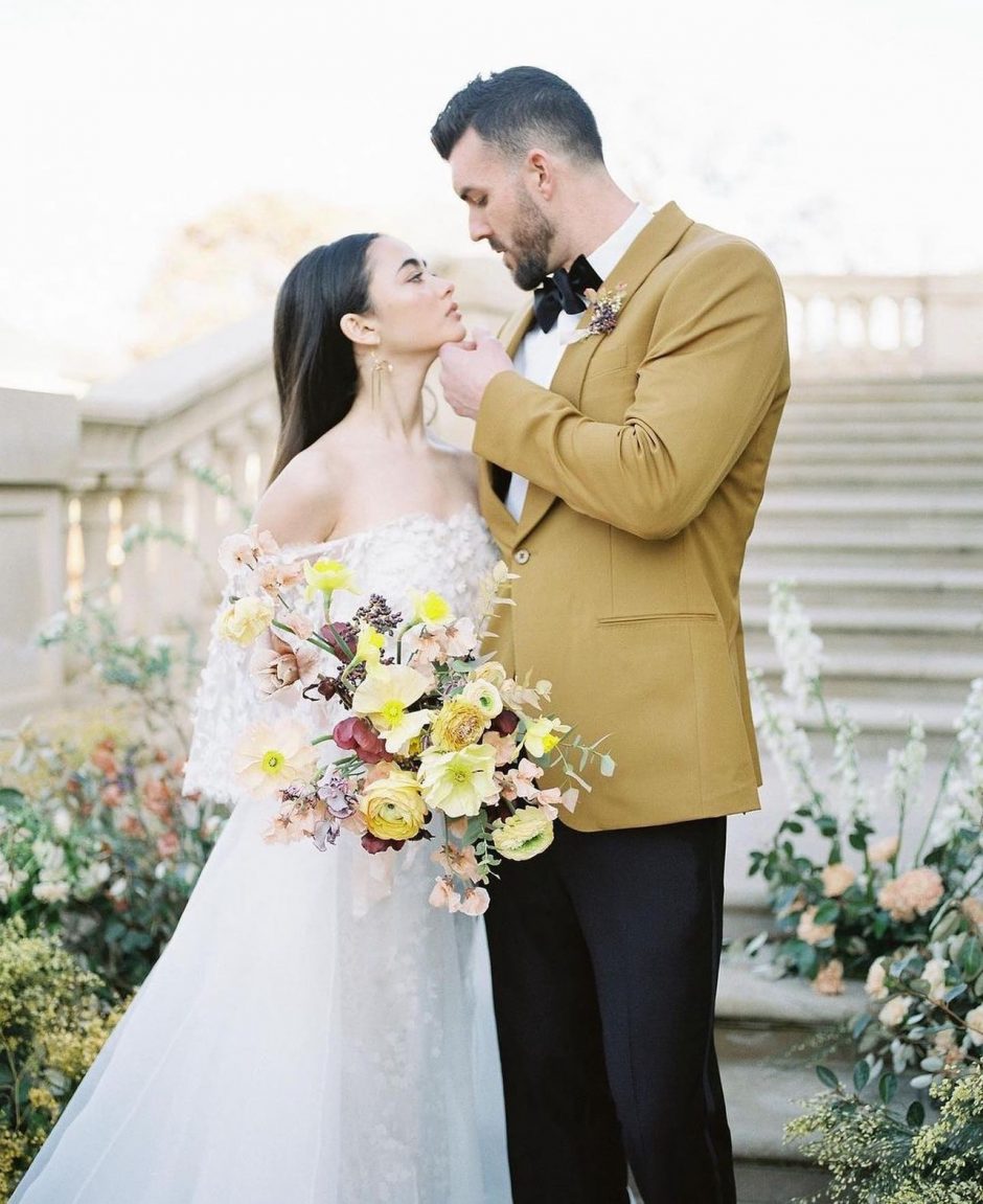 Newlywed couple holding bouquet of neutral-tone flowers.