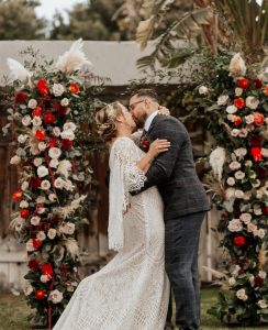 Newlywed couple with red and cream flowers for bohemian wedding theme.