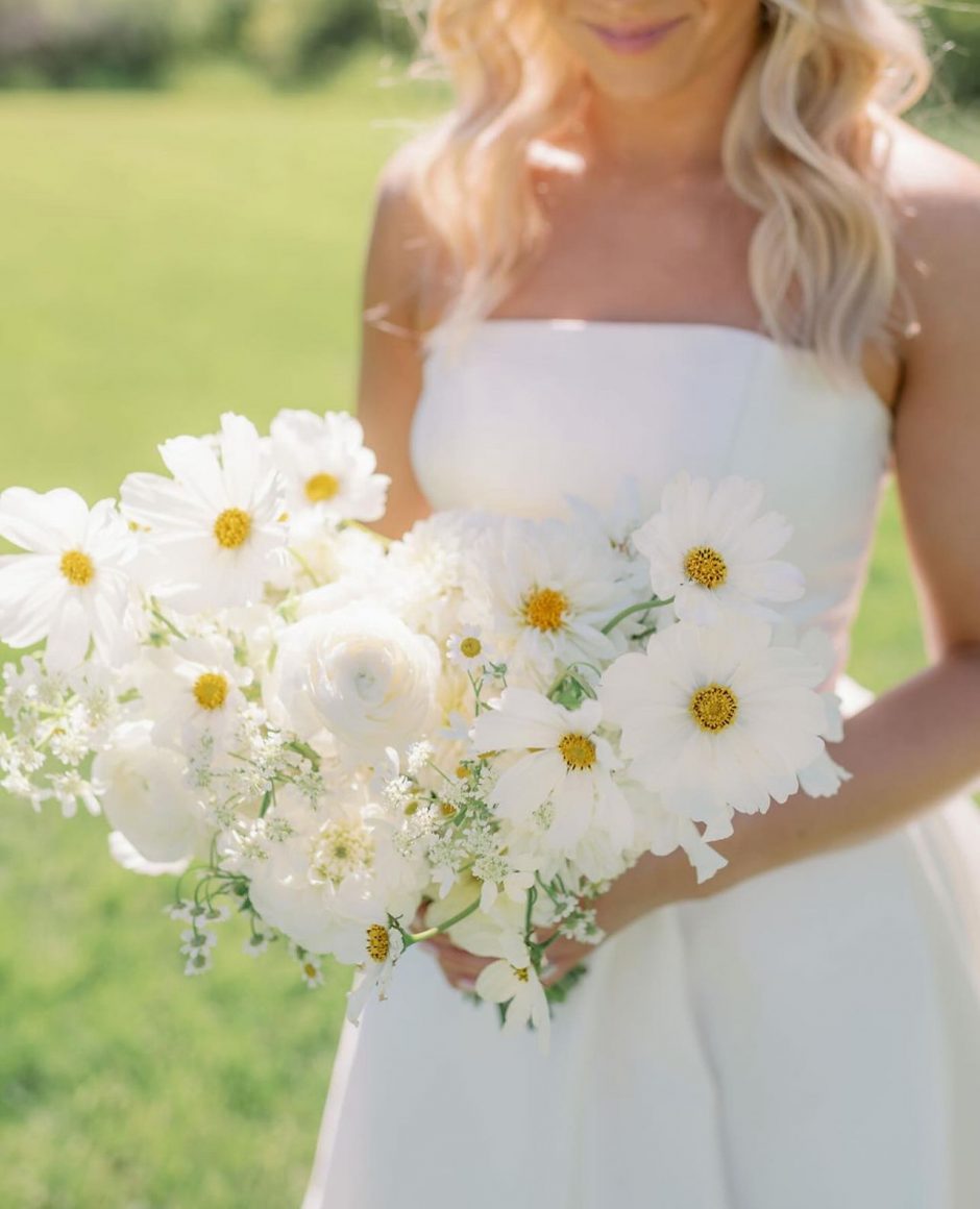 Bride holding bouquet with white ranunculus, daisies, and baby's breath.