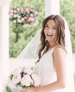 Bride holding wedding bouquet with pink roses, peonies, and ranunculus.