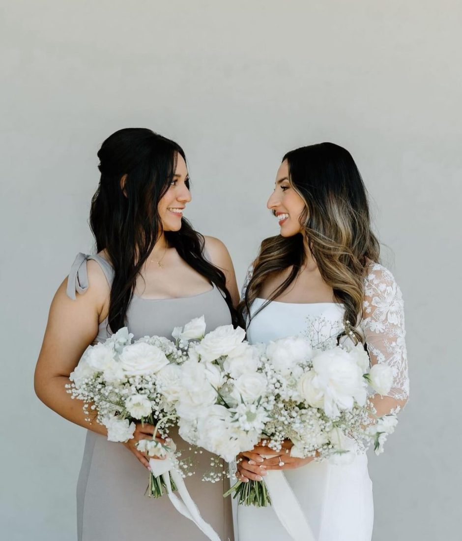 Bride and bridesmaid with white floral arrangements.