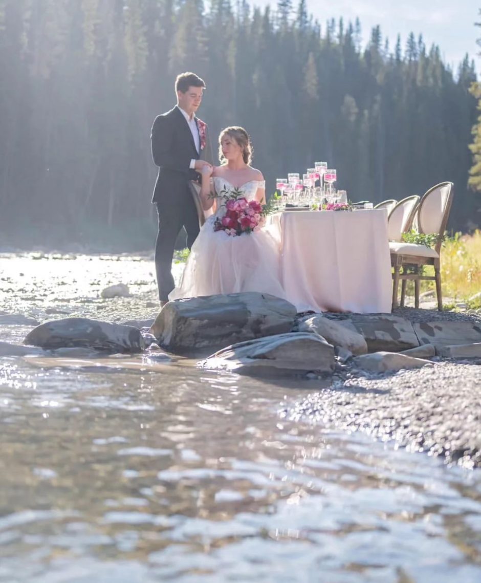 Newlywed couple with pink wedding flowers at riverside wedding.