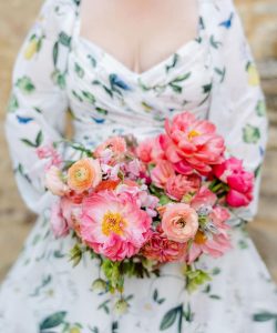 Bride holding wedding bouquet with coral charm peonies.