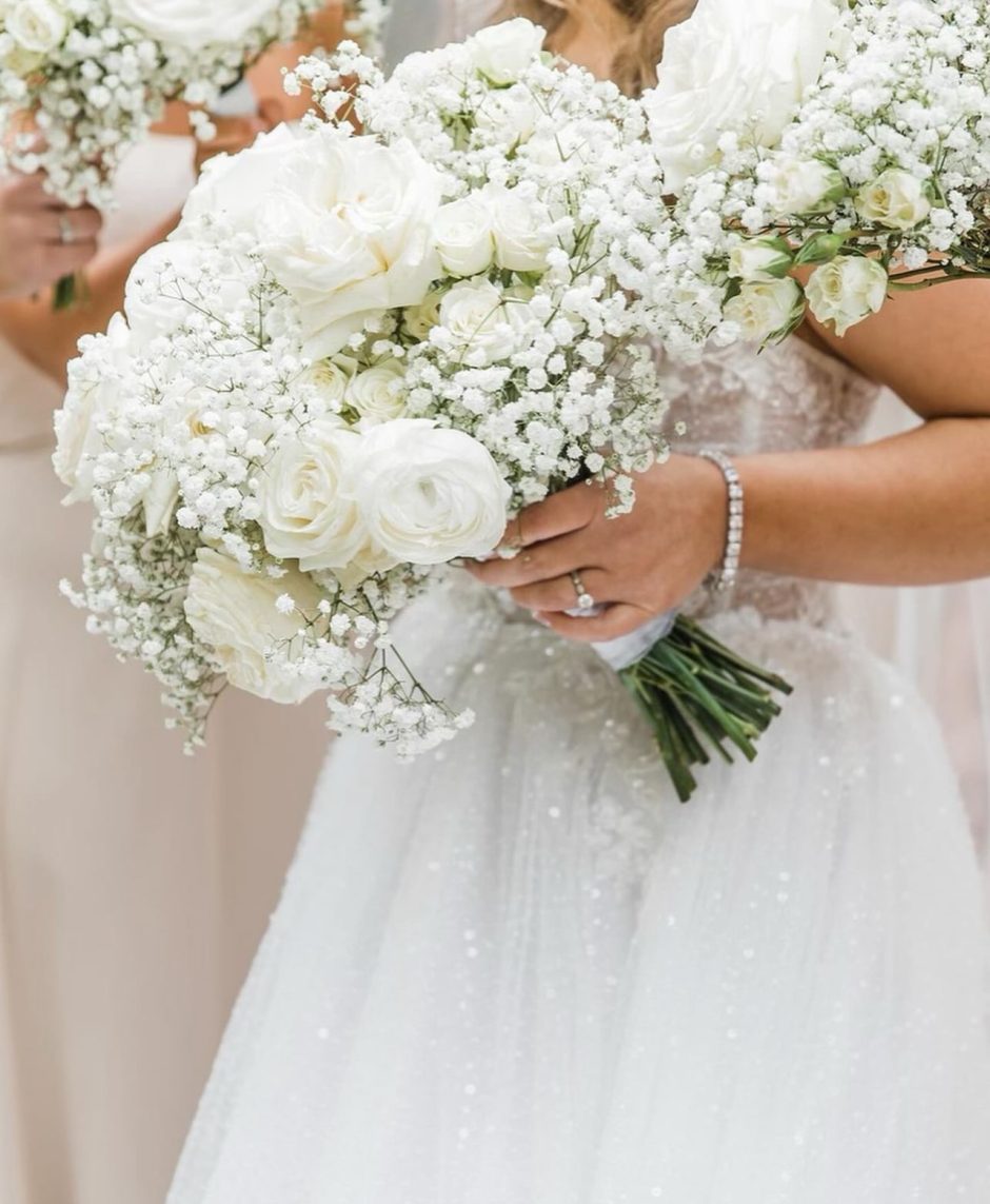 Bride holding bouquet with white roses and baby's breath.