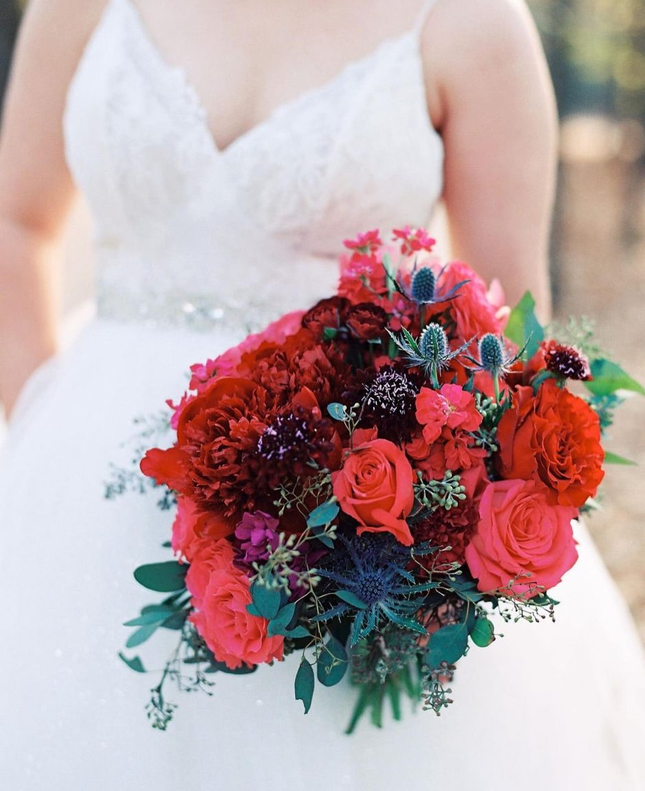Bride with bouquet of thistle, red flowers, and burgundy flowers.