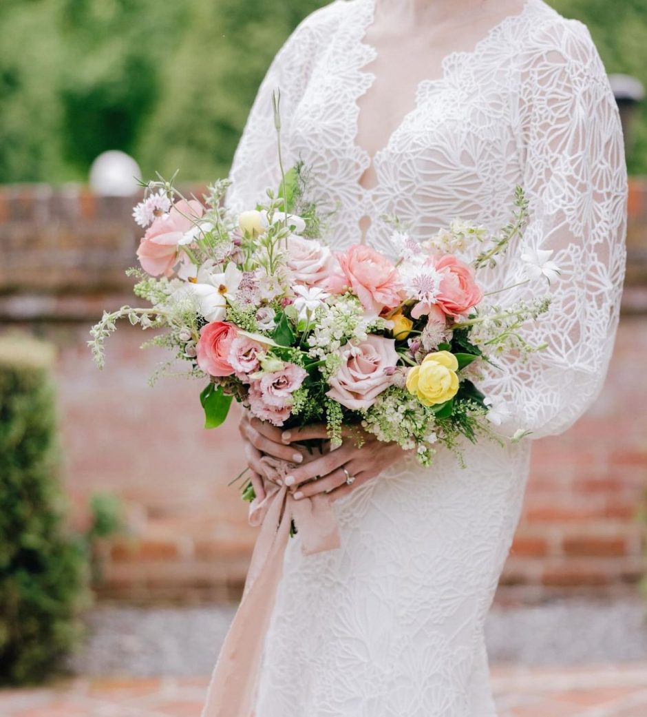 Woman holding bouquet of flowers with blush roses and lush greenery.