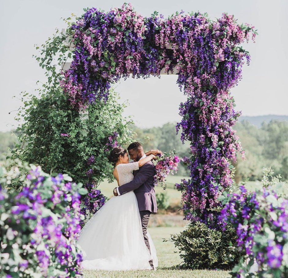 Newlywed couple surrounded by purple wedding flowers.
