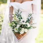 Bride holding bouquet of white roses, white anemone, and ruscus.