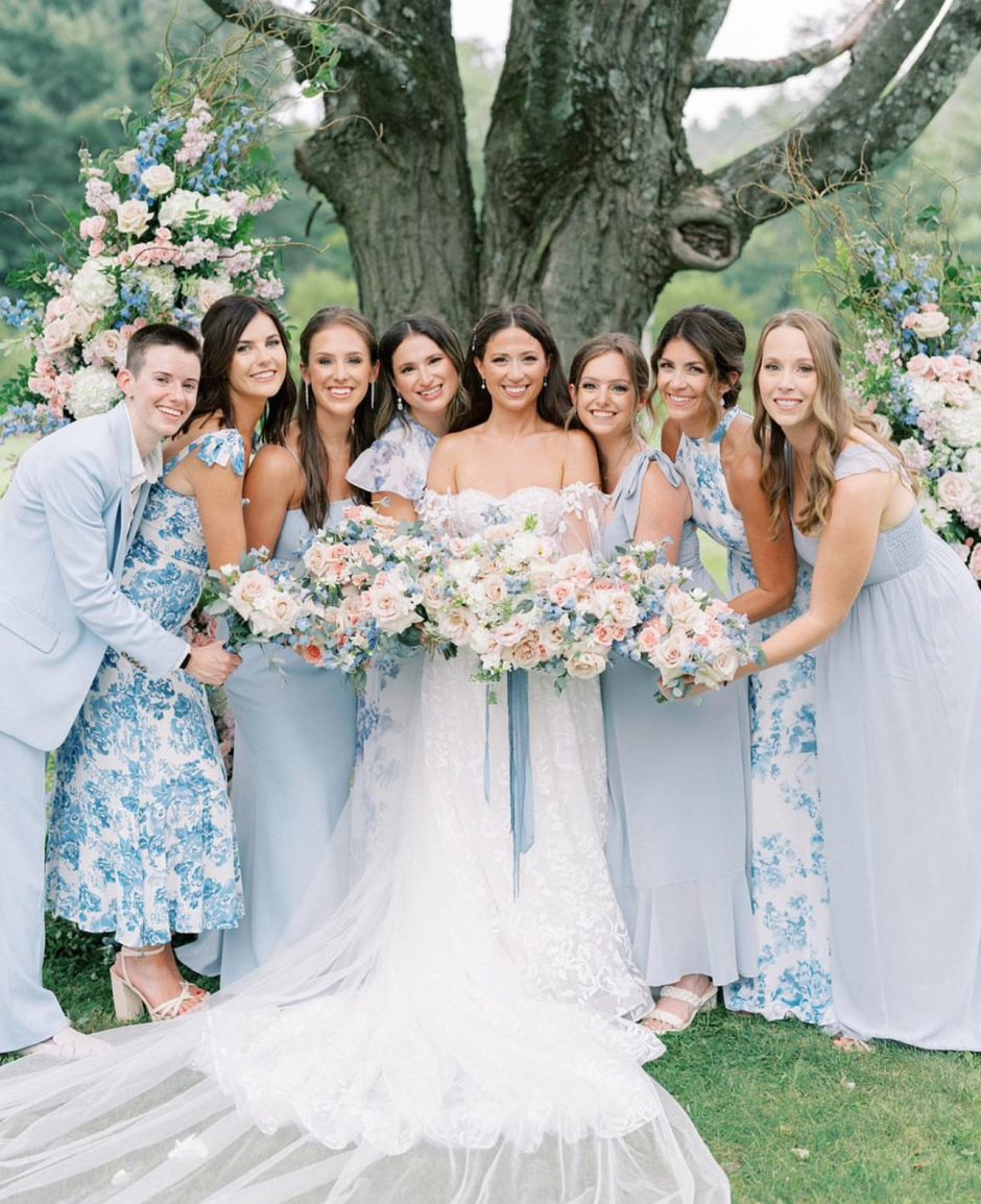 Bride and bridesmaids with bouquets with light blue, light pink, and white flowers.