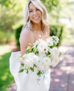Bride holding wedding bouquet with varieties of white flowers.