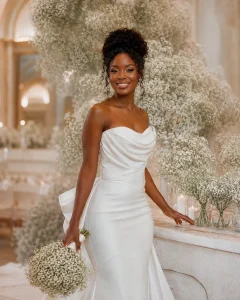 Black bride in pearl ivory gown holding baby’s breath bouquet beside elegant baby’s breath wedding arrangements in a romantic ballroom.