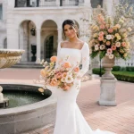 Iberian bride with warm-toned skin holding a Butterfly Ranunculus bouquet in blush, peach, cream, apricot, coral, and buttery yellow at an Ashford Estate-inspired wedding, showcasing airy branching blooms and elegant garden-style floral design.