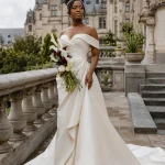 West African bride in a champagne gown holding white and burgundy calla lilies on a grand terrace at Biltmore Estate in Asheville.