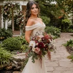 Lebanese bride holding a trendy fall wedding bouquet with burgundy dahlias, garden roses, orchids, ranunculus, and cascading greenery.